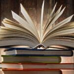 An open book resting on a stack of closed books against a wooden background.