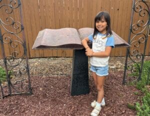 Girl smiling beside large open book sculpture